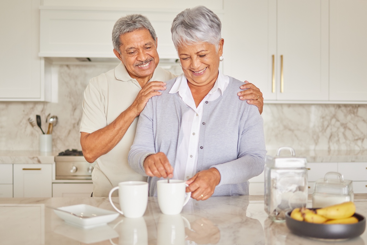 Two people smiling looking at their coffee in a kitchen